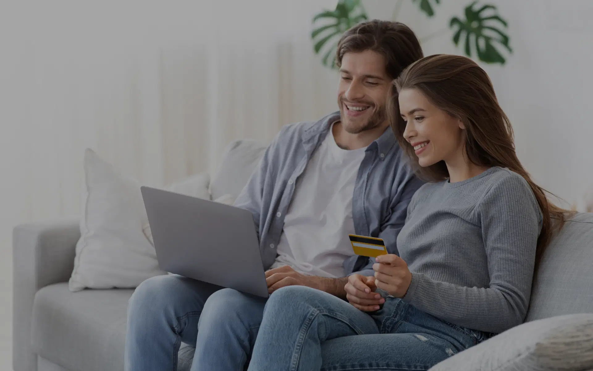 A couple using a laptop and holding a credit card in the girl's hand at home.